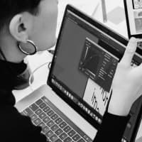 A person with dark hair viewing code or design software on a laptop in black and white