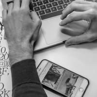 Hands typing on a laptop keyboard with a smartphone visible on the desk, captured in black and white