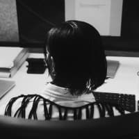 The back of a person with short dark hair seated at a computer workstation, shown in black and white